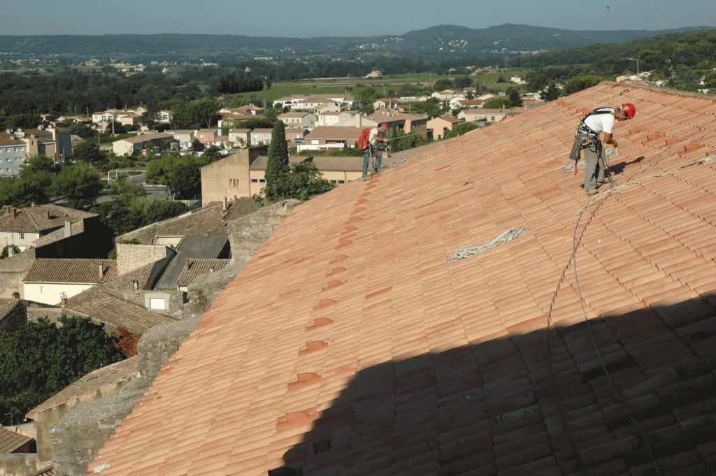 Deux cordistes sur la toiture en tuiles neuves de l’église, au-dessus du village