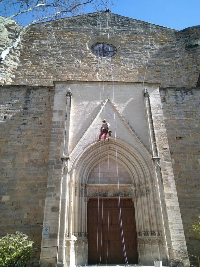 Cordiste en rappel sur la façade de l’église Notre-Dame-la-Neuve, à Laudun-l’Ardoise