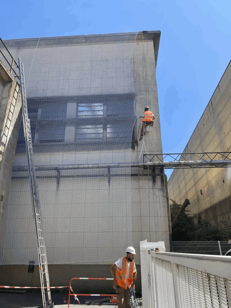 Cordiste en descente posant un filet de sécurisation sur une façade industrielle