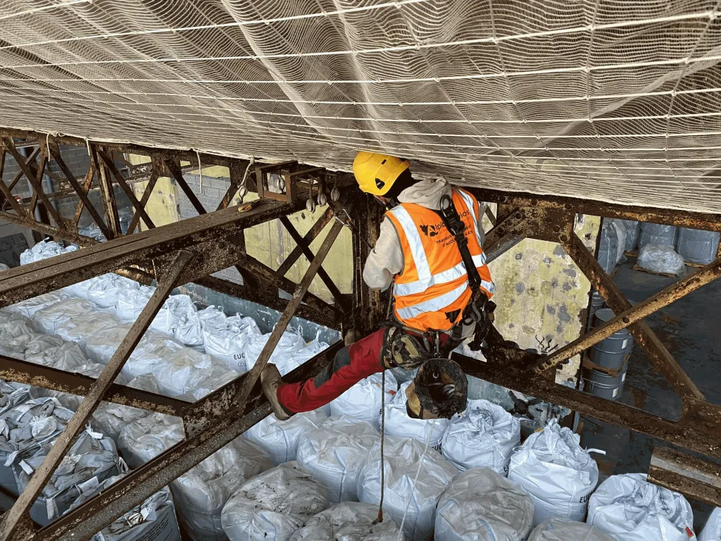 Cordiste posant un filet de sécurité sous la charpente métallique d’un hangar