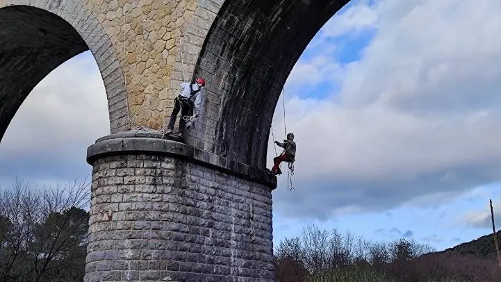 Deux cordistes suspendus sous l’arche d’un viaduc en maçonnerie