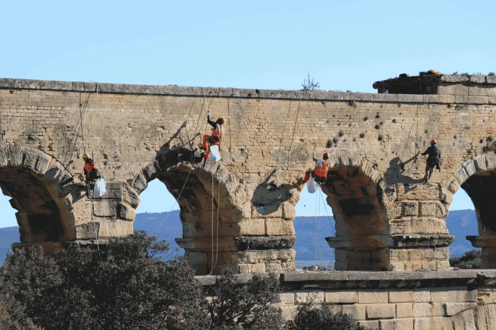 Quatre cordistes en dévégétalisation sur les arches du pont du Gard