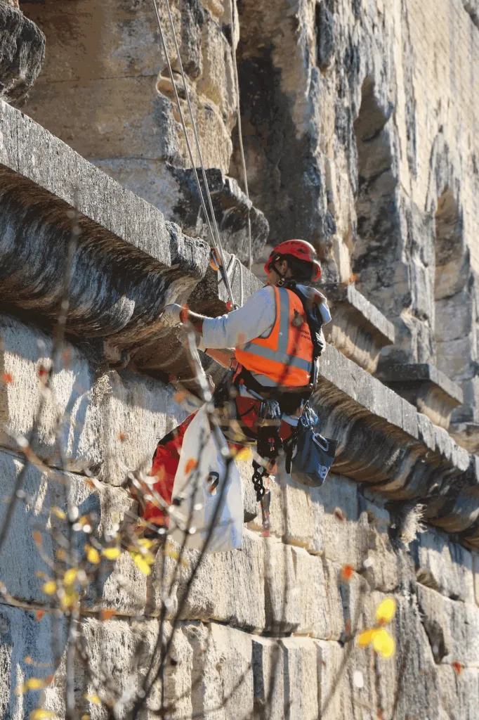 Cordiste nettoyant une corniche du pont du Gard, sac de déchets à la ceinture