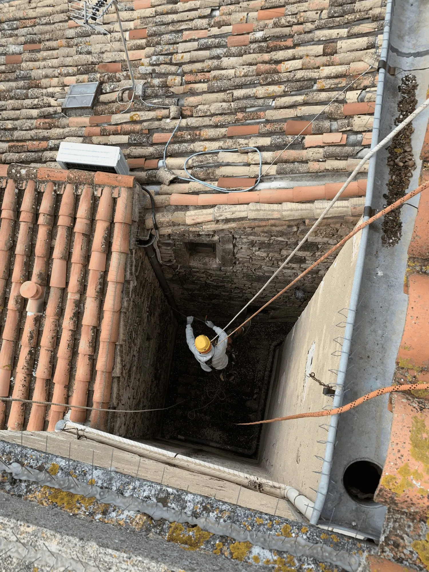 Cordiste descendu dans un puits de lumière étroit, entre deux toitures de village