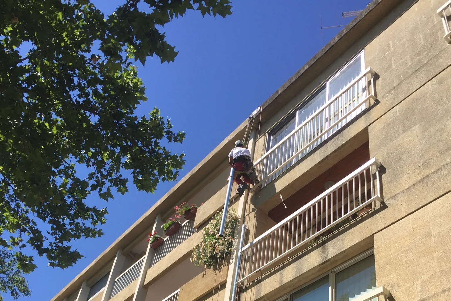 Cordiste remplaçant une descente d’eaux pluviales en zinc sur la façade d’un immeuble à Nîmes